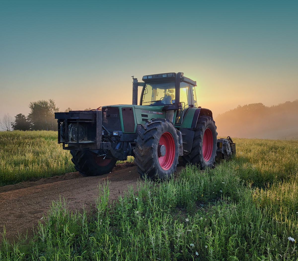 Traktor obrađuje poljoprivredno zemljište u svjetlu zalazećeg sunca.